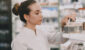 Medicine, pharmaceutics, health care and people concept. Female pharmacist taking medications from the shelf.